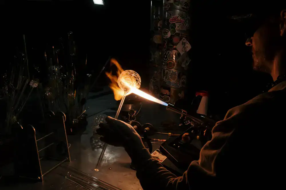 Expert glassblower guiding a student with a blowpipe
